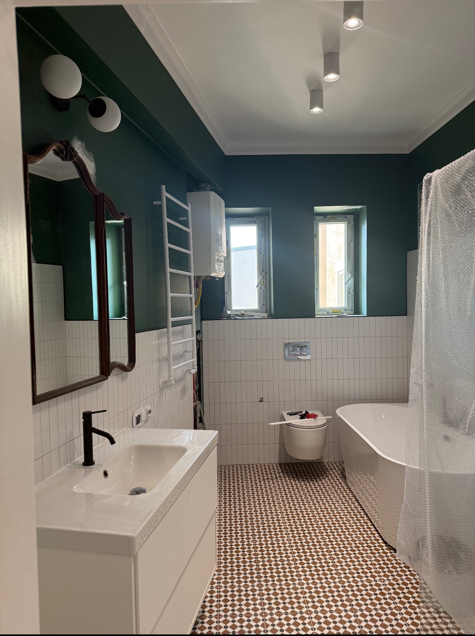 Nowoczesna łazienka po remoncie: białe płytki, ciemnozielone ściany, wzorzysta podłoga, umywalka z szafką, wanna i okna. Elementy wykończeniowe.