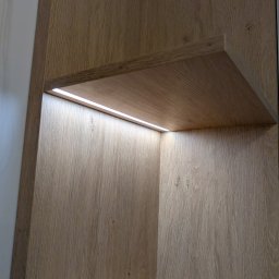 Vihajster - Bartłomiej Jaskuła - Półka z oświetleniem LED wewnątrz szafy o jasnym, drewnopodobnym wykończeniu. Minimalistyczny design, ciepłe światło podkreśla strukturę drewna.