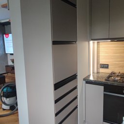 Vihajster - Bartłomiej Jaskuła - Szara zabudowa kuchenna z szafkami i szufladami z czarnymi uchwytami, oświetlenie LED pod szafkami, widok na płytę grzewczą i piekarnik. Nowoczesny design.