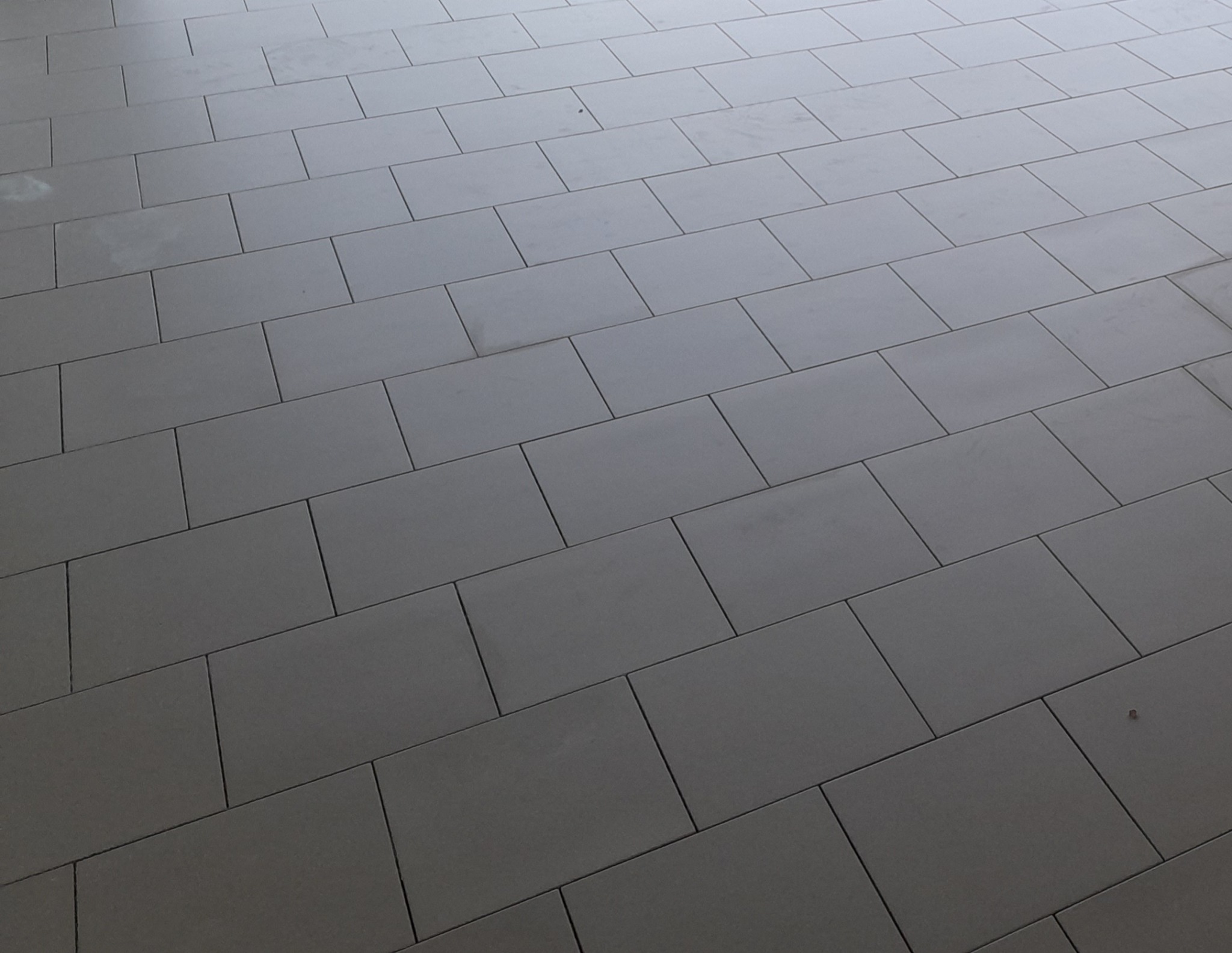 Ułożona pod kątem podłoga z szarych, prostokątnych płytek, widoczna z góry. Minimalistyczny wzór z fugami. Neutralna kolorystyka.