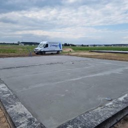 Usługi Ogólnobudowlane Błażej Kański - Świeżo wylany fundament pod budynek, z widocznym firmowym vanem w tle na tle krajobrazu polnej działki w słoneczny dzień.