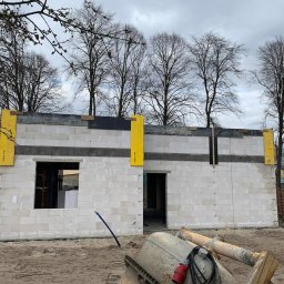 Usługi Ogólnobudowlane Błażej Kański - Wznoszenie murów domu z betonu komórkowego z widocznym oknem i otworem drzwiowym. Szalunki pionowe w kolorze żółtym. Na pierwszym planie betoniarka.