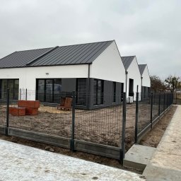 Usługi Ogólnobudowlane Błażej Kański - Nowoczesne domy jednorodzinne z szarymi dachami, widok z zewnątrz, ogrodzenie panelowe z podmurówką, elementy małej architektury ogrodowej, pochmurne niebo.
