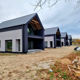 Usługi Ogólnobudowlane Błażej Kański - Szereg identycznych, nowoczesnych domów z dwuspadowymi dachami i ciemnymi elewacjami, widok z zewnątrz, jesienne liście na ziemi, pochmurne niebo.