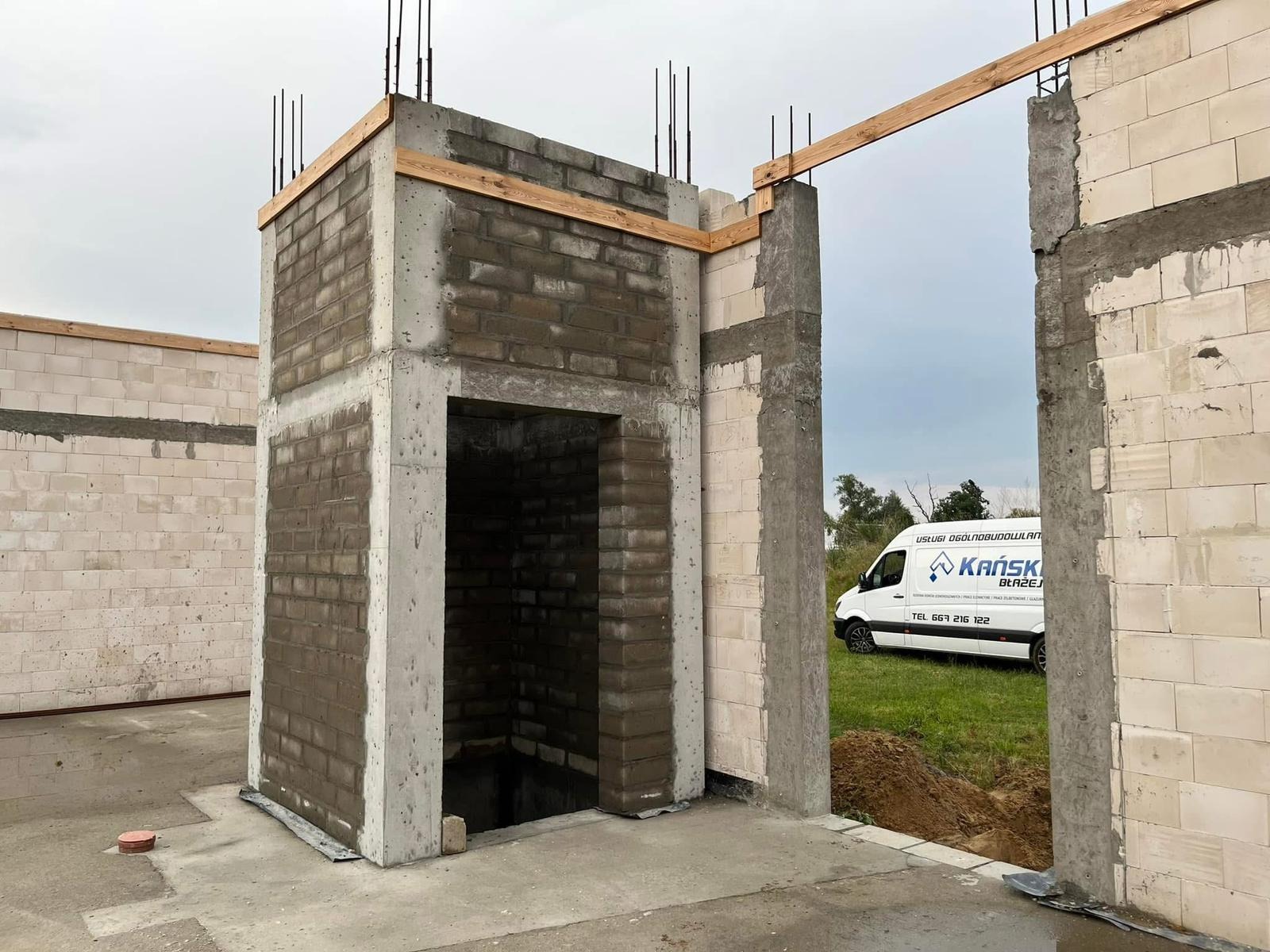 Surowy stan budynku z betonu komórkowego i cegły silikatowej w Nowym Tomyślu. Widoczne zbrojenia, drewniane elementy szalunku i firmowy bus w tle.