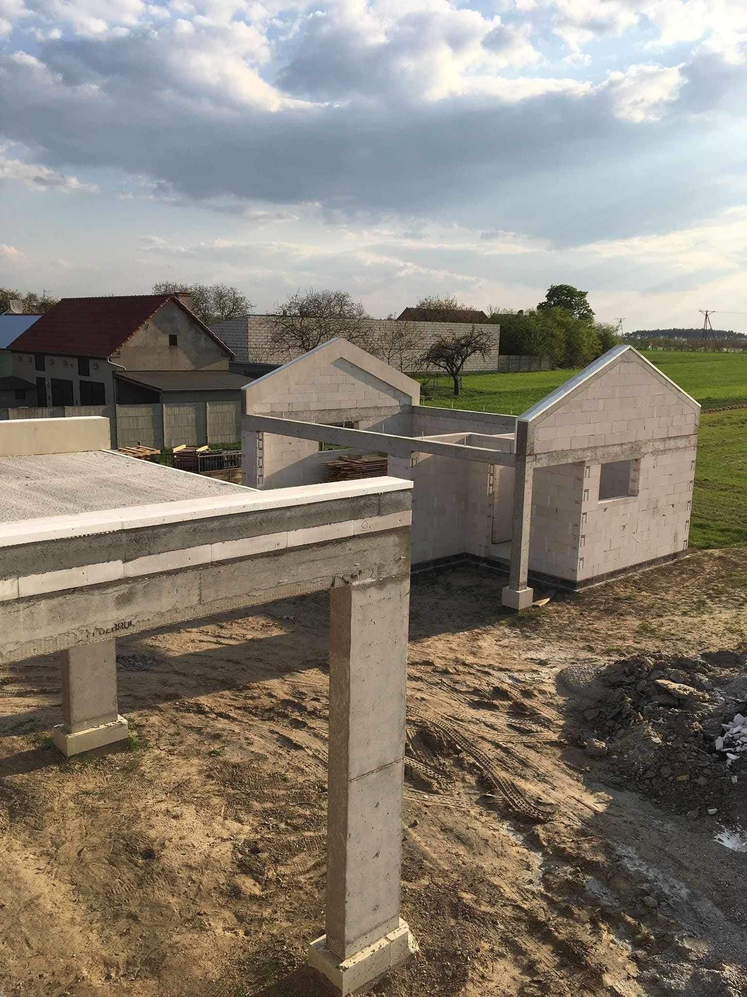 Wznoszenie surowego stanu domu z betonu komórkowego, widok z góry na plac budowy. Częściowo ukończona konstrukcja, betonowe słupy i strop.