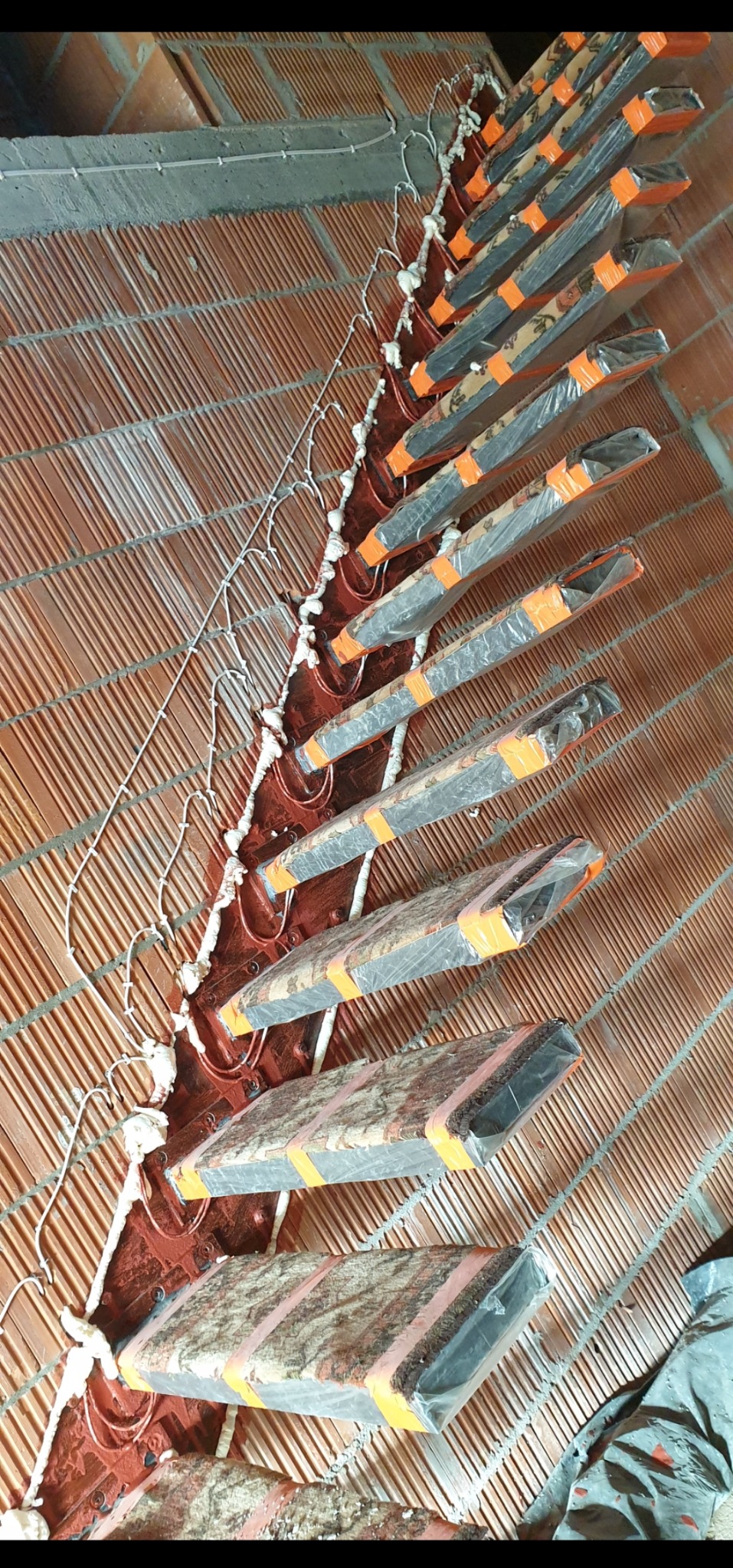 Montaż ocieplenia od wewnątrz: styropianowe płyty zabezpieczone folią, mocowane do ściany z cegły za pomocą pianki montażowej i stalowych kotew. Widoczne przewody elektryczne.