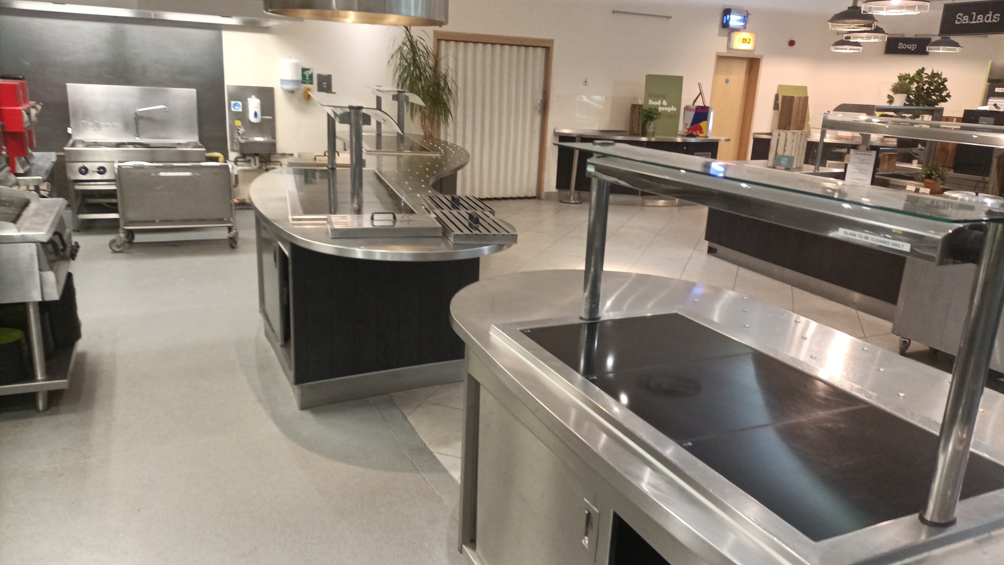 Profesjonalna kuchnia gastronomiczna z nierdzewnymi stanowiskami do wydawania posiłków, widok z perspektywy posadzki, oświetlenie sufitowe.