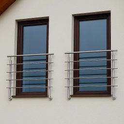 Solidpro - Dwa okna z brązowymi ramami zabezpieczone nowoczesnymi, poziomymi balustradami ze stali nierdzewnej, zamocowanymi na zewnątrz budynku o jasnej elewacji.