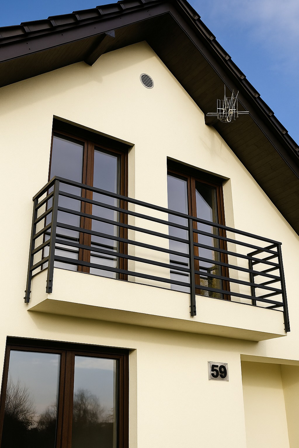 Elewacja domu z beżową farbą, ciemnobrązowym dachem i oknami. Na piętrze balkon z czarną, metalową barierką o minimalistycznym designie.