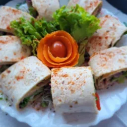 Dekoracyjnie ułożone tortille z warzywami i pomidorową ozdobą na białym talerzu z zielonymi akcentami, prezentacja cateringu.