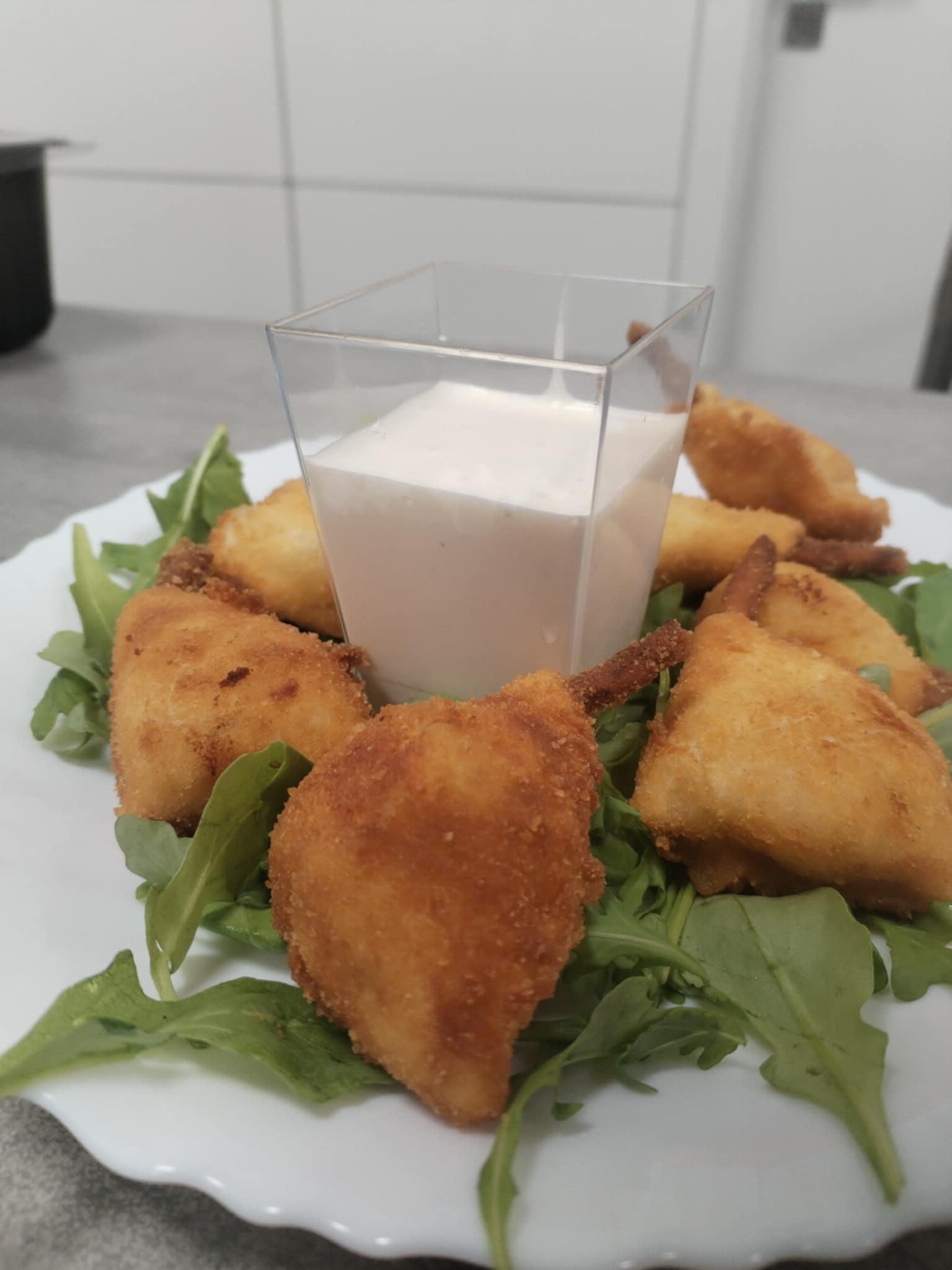 Elegancko podane, smażone pierożki na rukoli z sosem w kwadratowym naczyniu na białym talerzu. Profesjonalny catering.