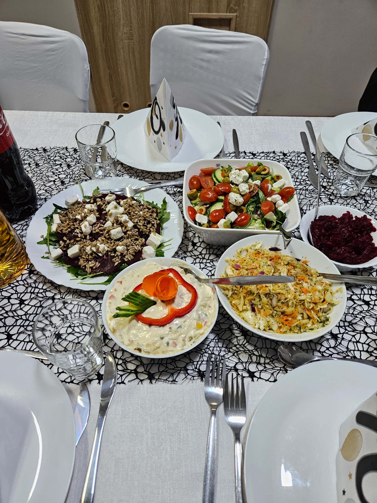 Uroczysty stół z różnorodnymi sałatkami, dekoracjami i napojami, przygotowany na przyjęcie. Dekoracyjny bieżnik z motywem pajęczyny.