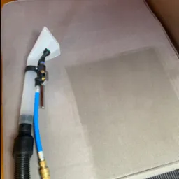 Fragment sofy z widocznym efektem czyszczenia tapicerki przy użyciu specjalistycznego sprzętu. Widoczna różnica w kolorze po praniu.