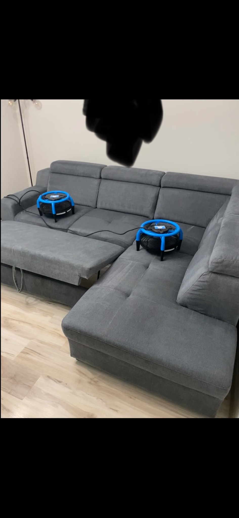 Szara, rozłożona sofa z dwoma urządzeniami do czyszczenia tapicerki. Widoczne kable i elementy wyposażenia wnętrza. Ujęcie z bliska, prezentujące proces czyszczenia.