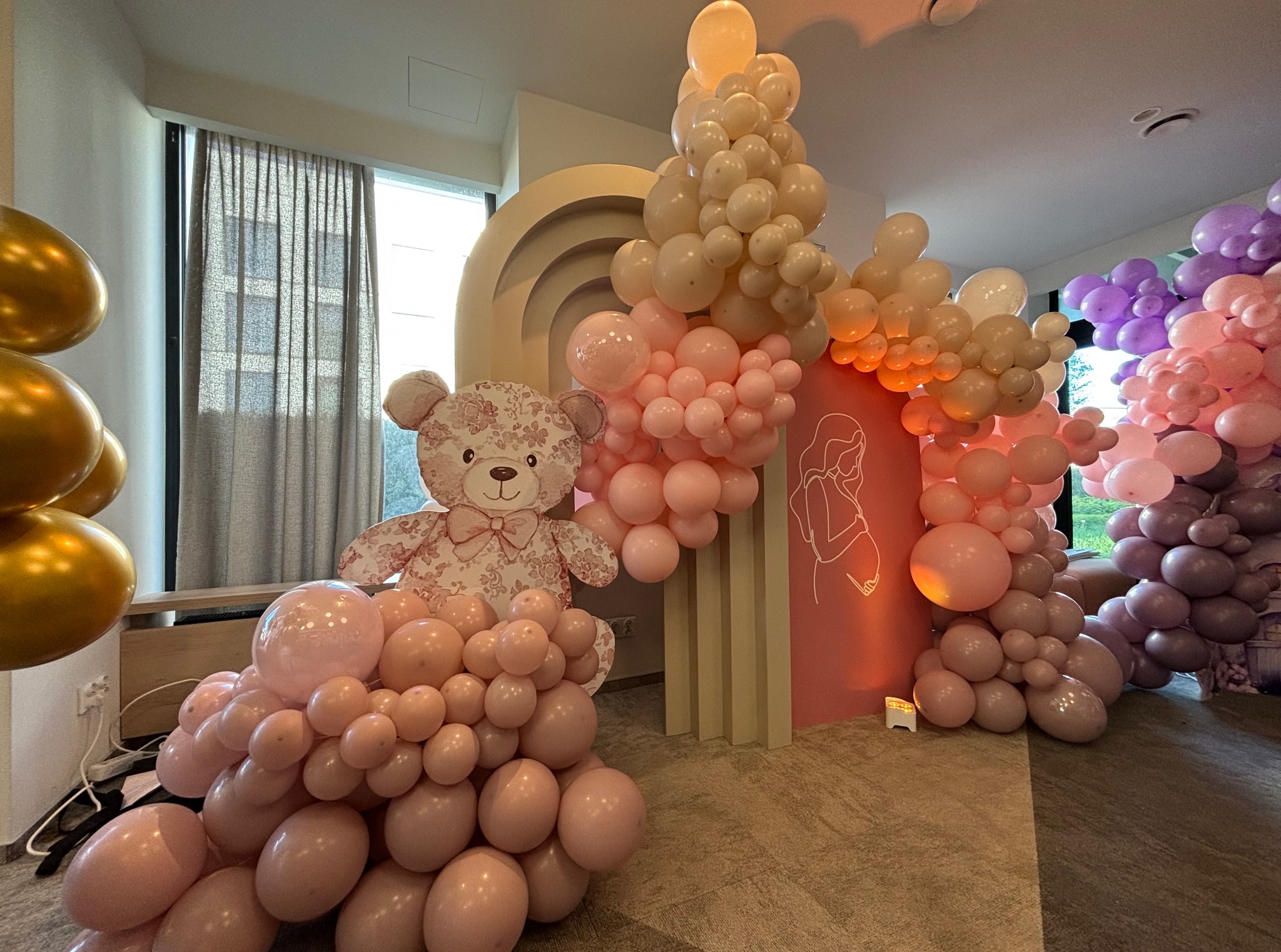Dekoracja balonowa z motywem misia i pastelowymi kolorami, idealna na baby shower, z rekwizytami i ścianką w tle.