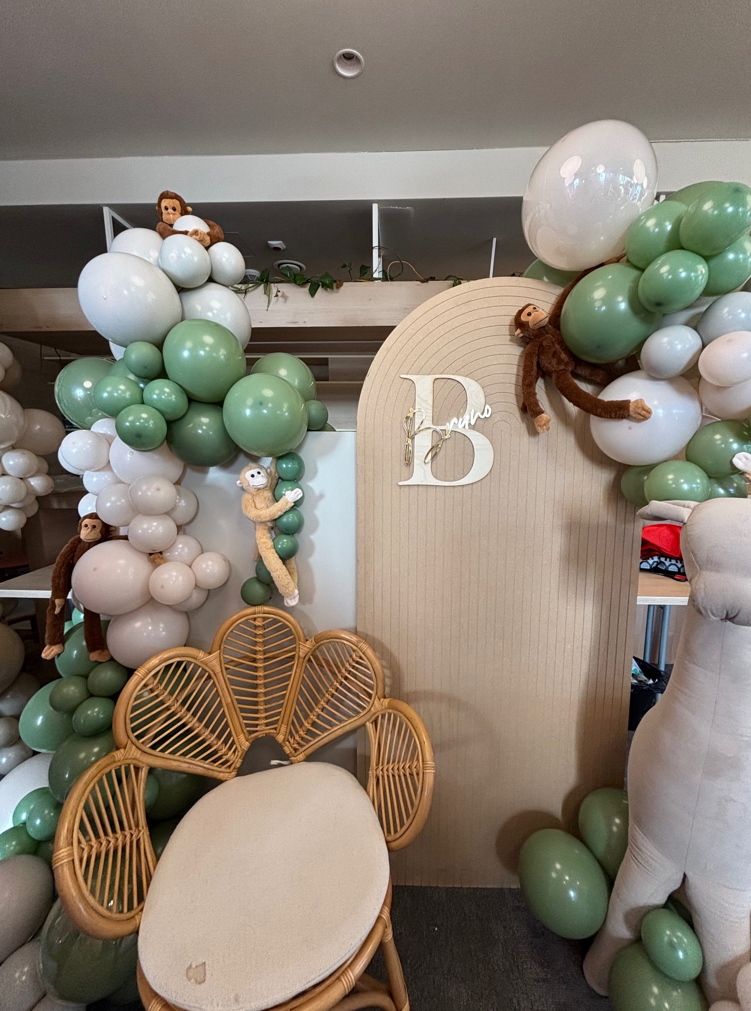 Udekorowana ścianka z balonami w odcieniach bieli i zieleni, pluszowe małpki i dekoracyjny napis z imieniem 'Borys' tworzą radosną scenografię.