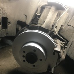 Auto-Pablo - Wymiana tarczy hamulcowej w samochodzie w Skokach. Nowa, srebrna tarcza zamontowana na tle zawieszenia pojazdu. Widoczne elementy układu hamulcowego.