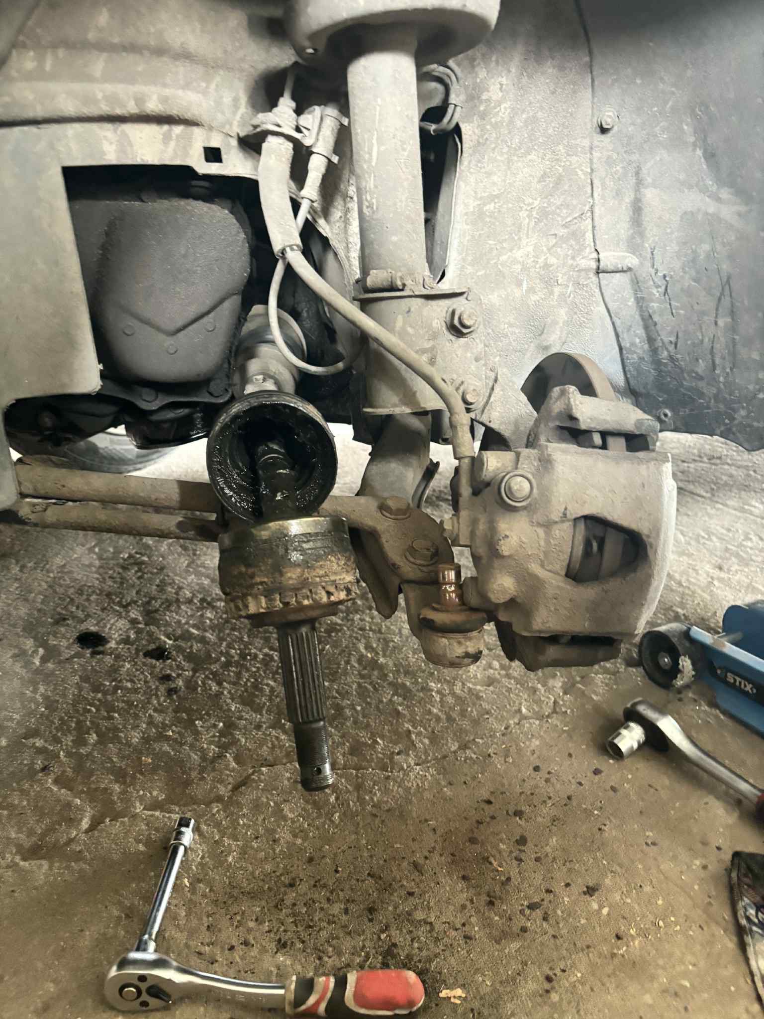 Rozłożony element zawieszenia samochodu z widocznymi narzędziami warsztatowymi na betonowej podłodze, ukazujący etap naprawy pojazdu.