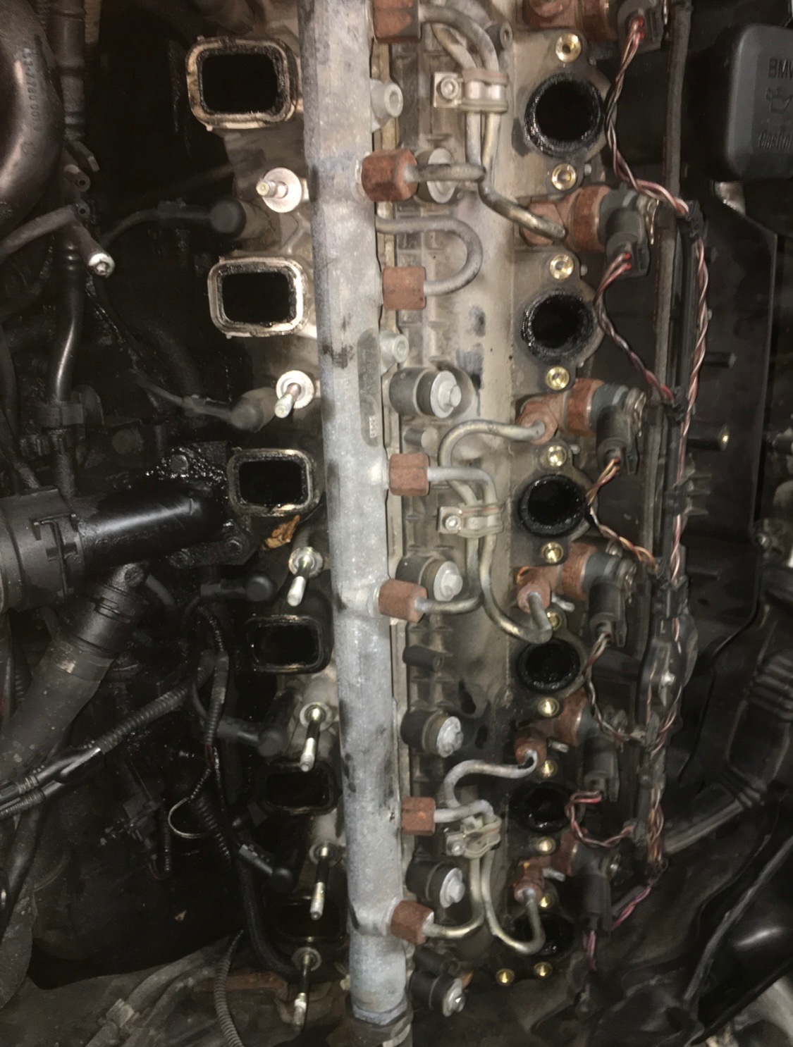 Brudny, zdemontowany silnik samochodowy z widocznymi przewodami, wtryskiwaczami i kolektorem, ukazujący skomplikowaną konstrukcję.