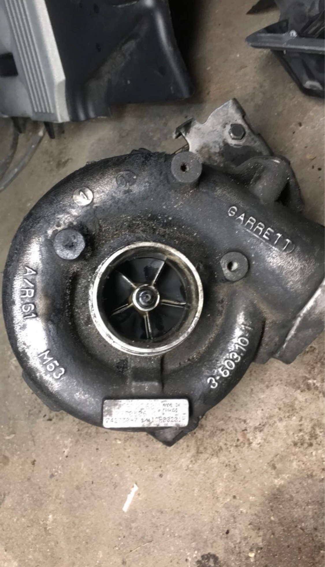 Używana turbosprężarka Garrett z widocznymi oznaczeniami modelu i numerami seryjnymi, leżąca na brudnej powierzchni. Widoczne ślady zużycia i oleju.