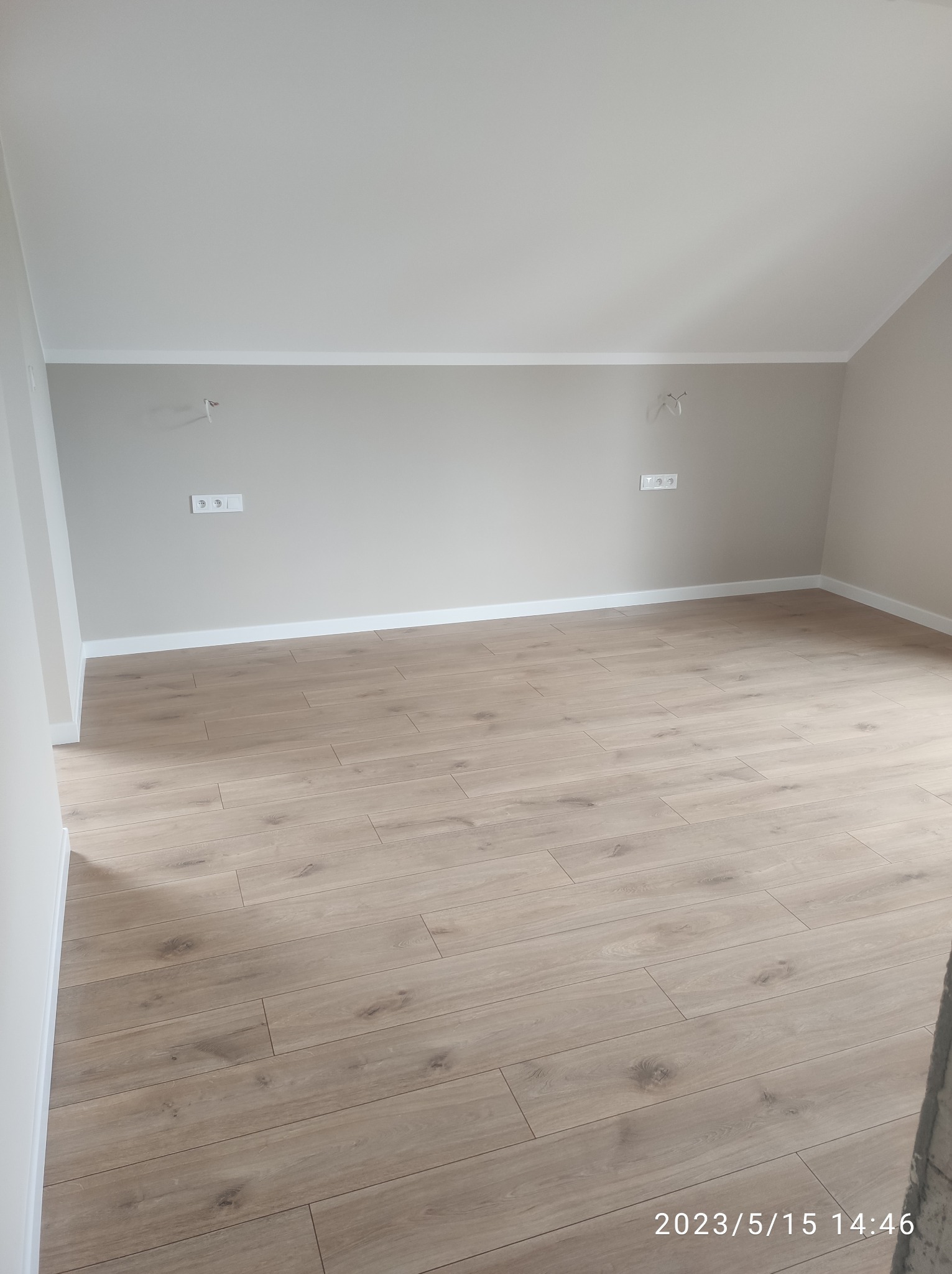 Jasne panele podłogowe w nowym pokoju z beżowymi ścianami, widoczne białe listwy przypodłogowe i gniazdka elektryczne. Ukończone wykończenie wnętrza.