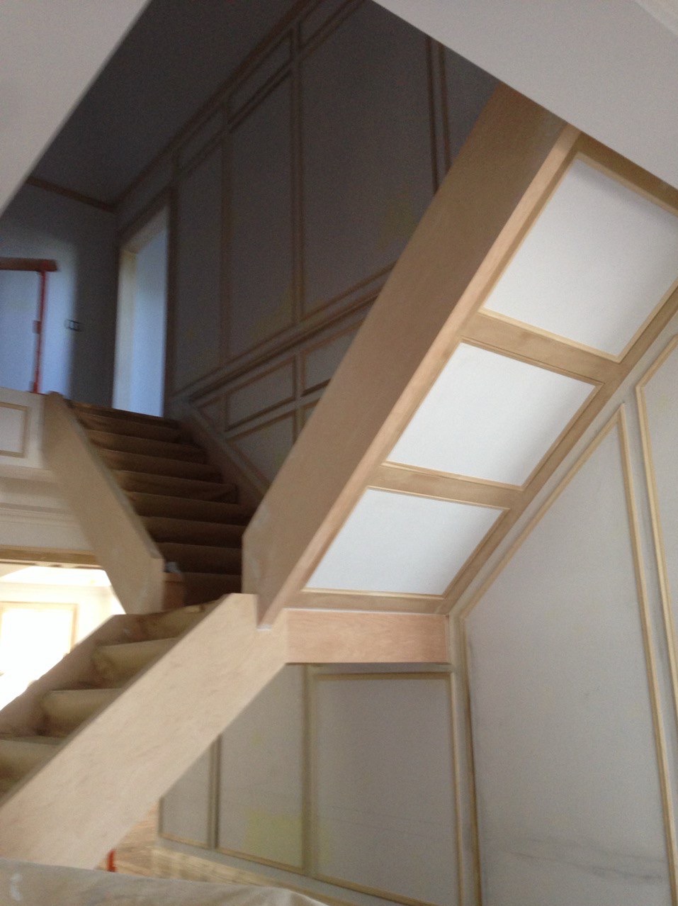 Klatka schodowa w trakcie wykańczania: surowe drewno schodów i balustrady kontrastuje z panelami ściennymi w stylu klasycznym, przygotowanymi do malowania.