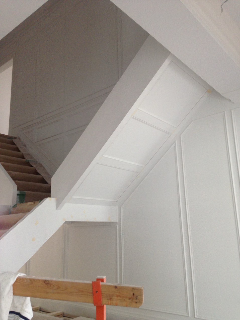 Białe, wykończone ściany klatki schodowej z dekoracyjnymi panelami i schodami w trakcie prac wykończeniowych. Widoczny fragment rusztowania.