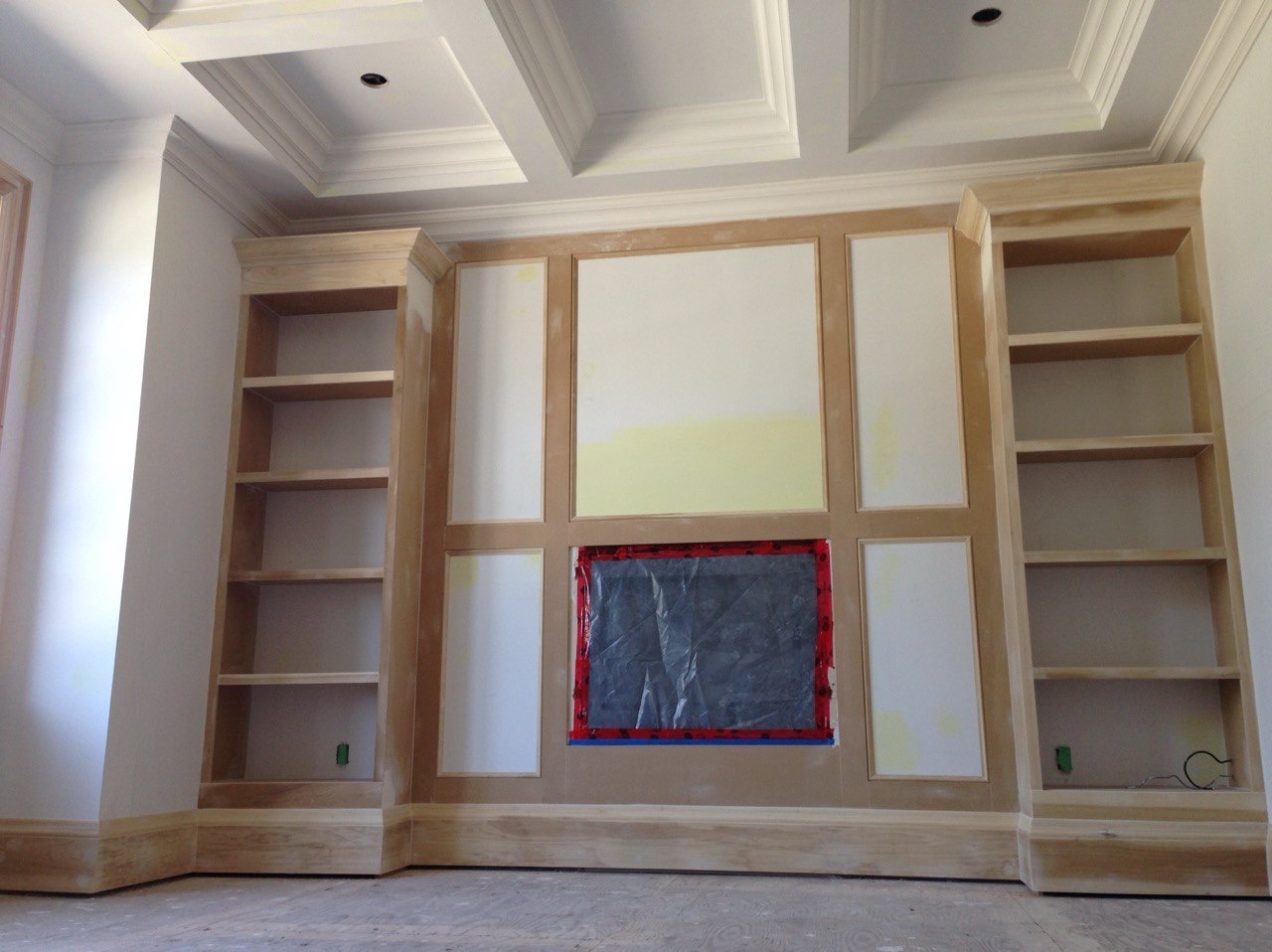 Ściana z regałami w trakcie przygotowania do malowania, zabezpieczone elementy, widoczne ślady szpachlowania i gruntowania. Detale wykończeniowe sufitu.