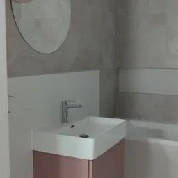 Nowoczesna łazienka z umywalką nablatową na szafce w odcieniach różu, okrągłe lustro i lampy wiszące. Płytki imitujące marmur na ścianach i podłodze.