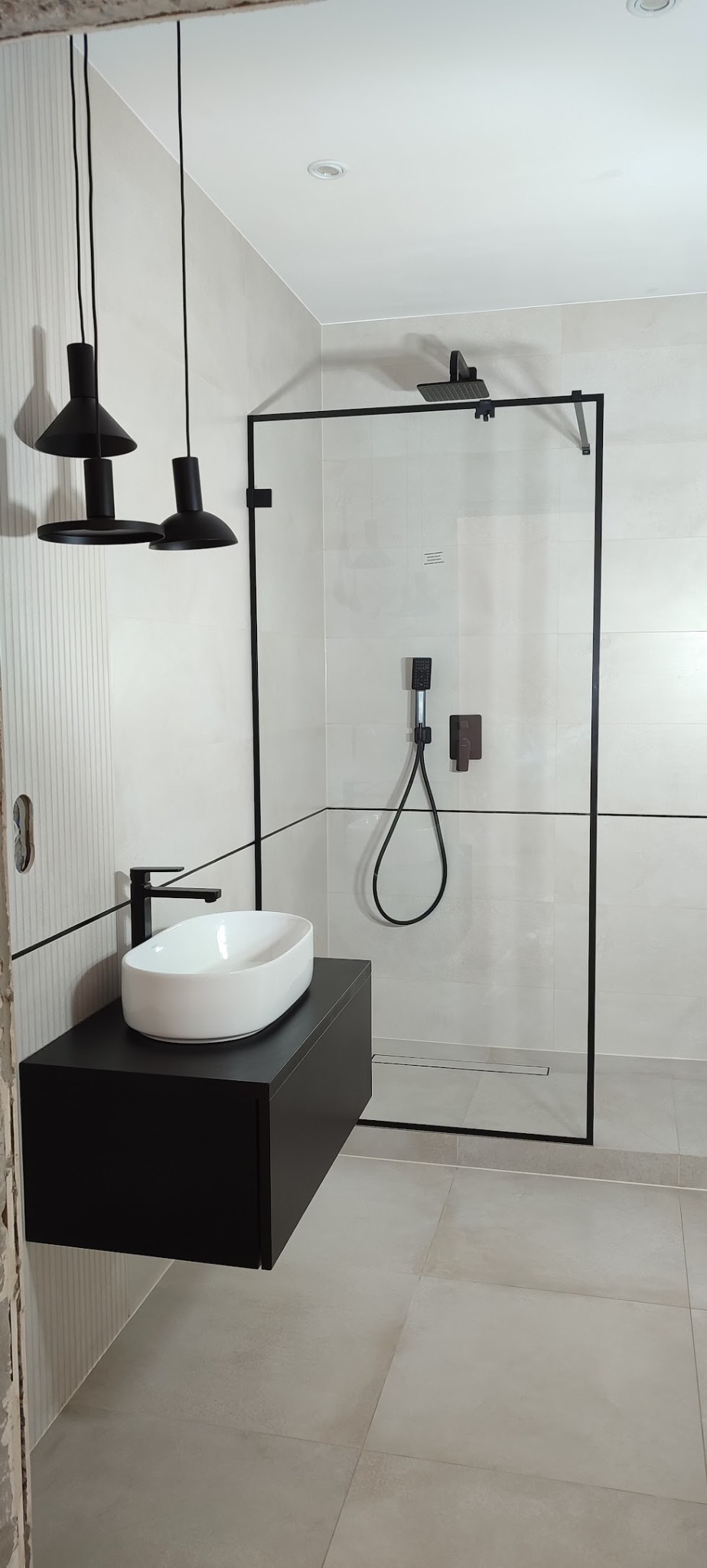 Nowoczesna łazienka z czarnymi akcentami: kabina prysznicowa typu walk-in, podwieszana szafka z białą umywalką i designerskie lampy wiszące.