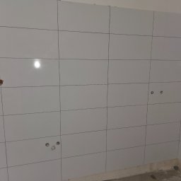 M&S GLOBAL SPÓŁKA Z OGRANICZONĄ ODPOWIEDZIALNOŚCIĄ - Wykafelkowana ściana w jasnych, kwadratowych płytkach z widocznymi otworami na instalacje. Świeżo położone kafelki na ścianie.