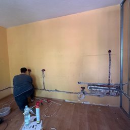 Paweł Jargon - Prace elektryczne we Wrocławiu: Instalacja przewodów w ścianie, widoczne puszki i narzędzia. Fachowiec w trakcie pracy, remont instalacji elektrycznej.