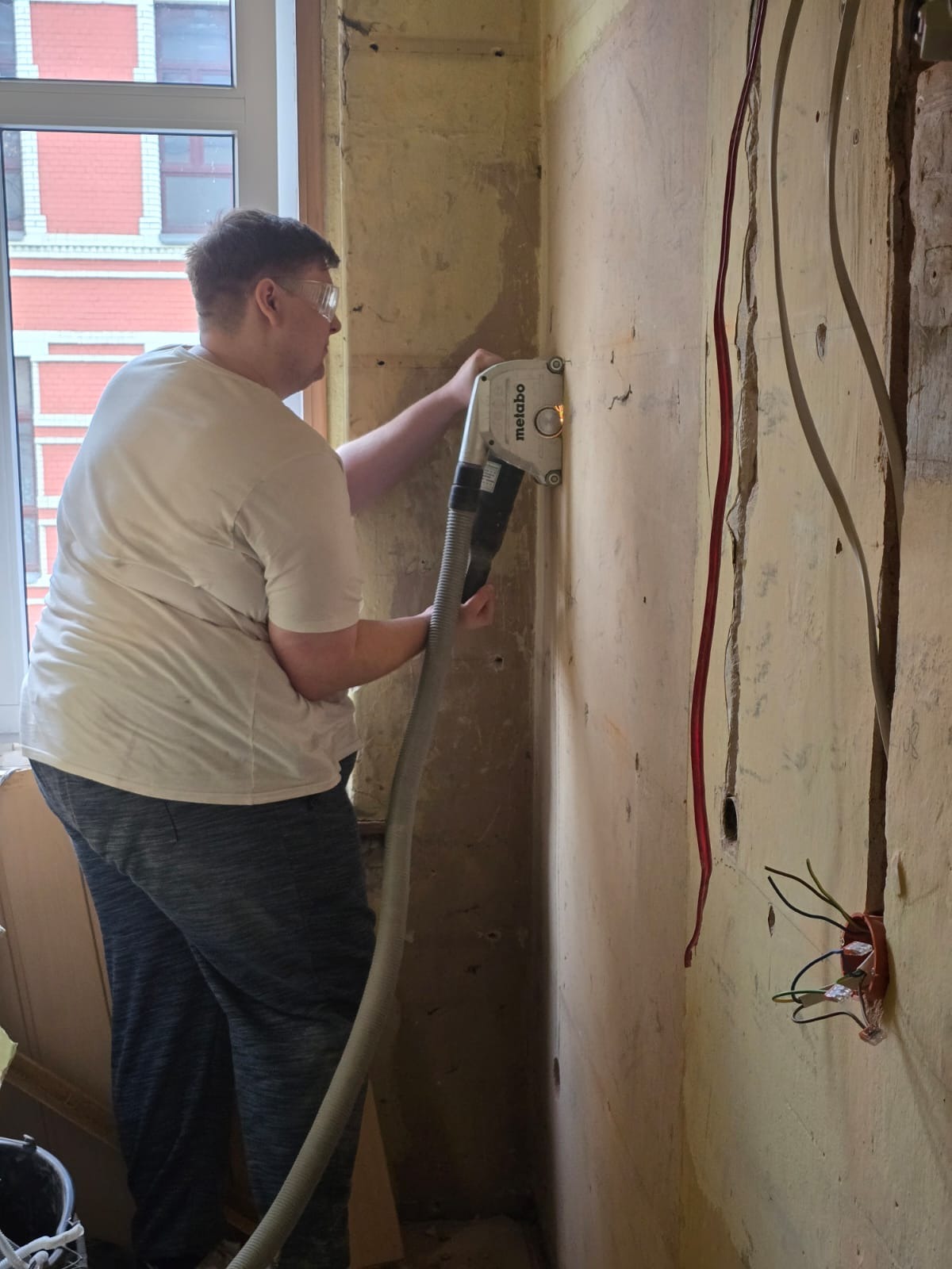 Prace przygotowawcze do instalacji elektrycznej: bruzdownica Metabo w użyciu, widoczne kable w ścianie, przygotowywane podłoże pod instalację. Praca w toku.