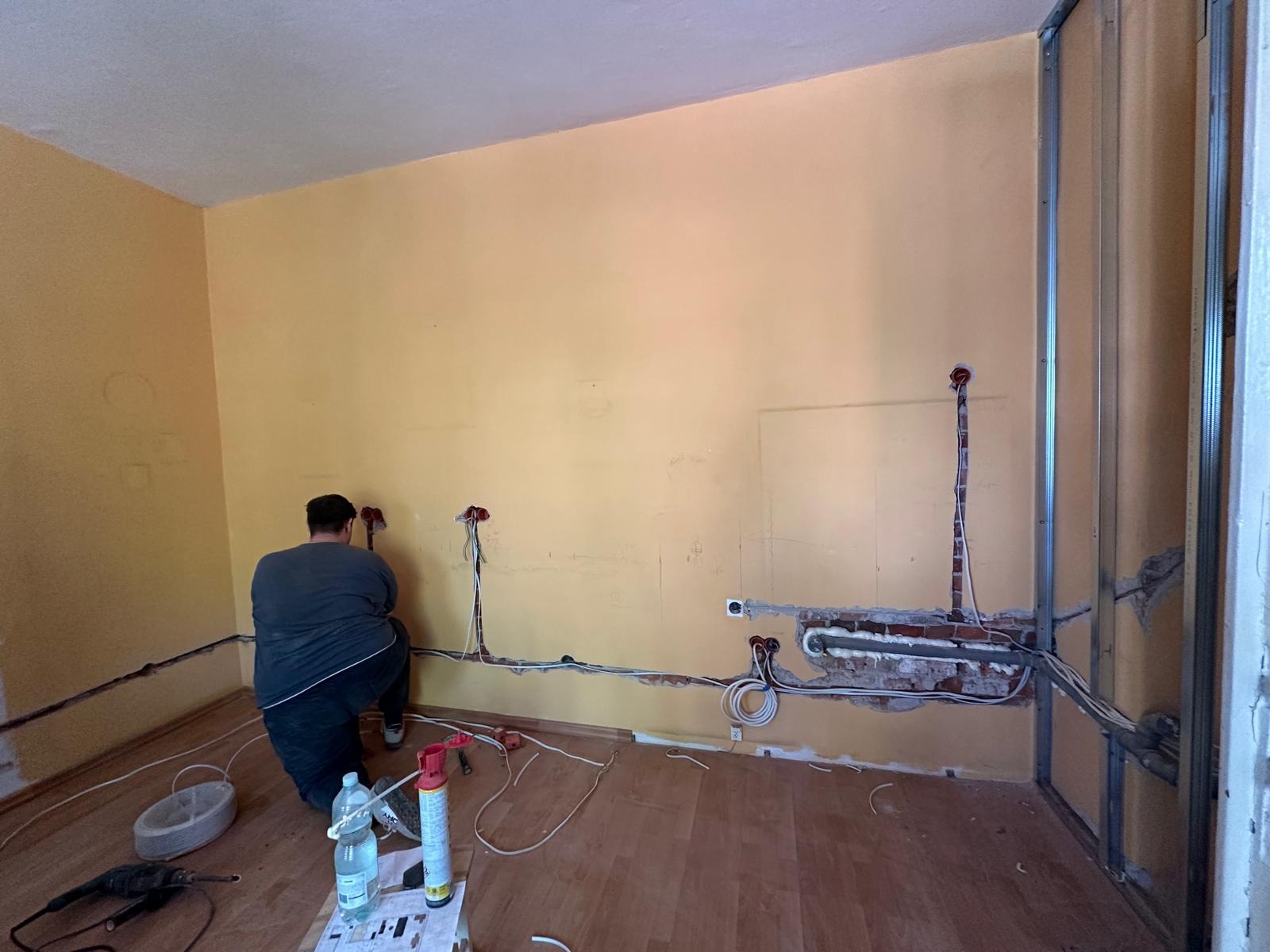 Prace elektryczne we Wrocławiu: Instalacja przewodów w ścianie, widoczne puszki i narzędzia. Fachowiec w trakcie pracy, remont instalacji elektrycznej.