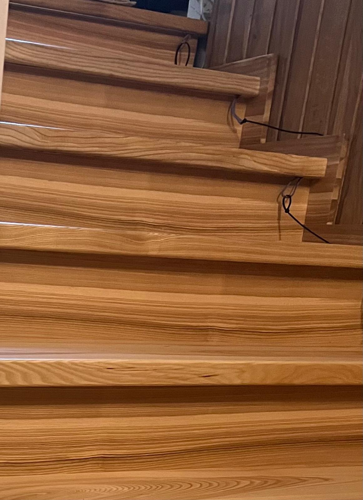 Jasne, drewniane schody wewnętrzne w trakcie montażu, widoczne z bliska. Detal wykończenia, naturalne usłojenie drewna, czarne elementy montażowe.