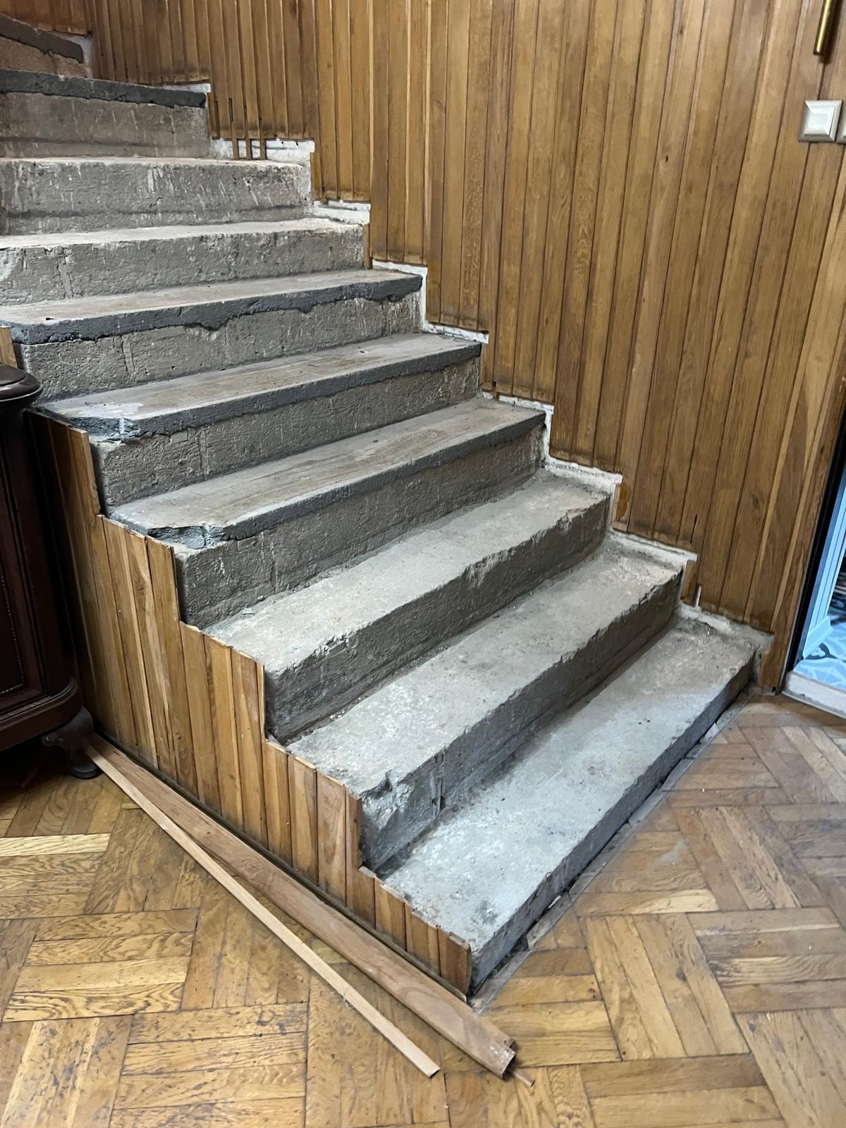 Betonowe schody w trakcie obudowy drewnianą boazerią, widoczne niedokończone elementy wykończenia i parkiet na podłodze. Ujęcie z dołu.