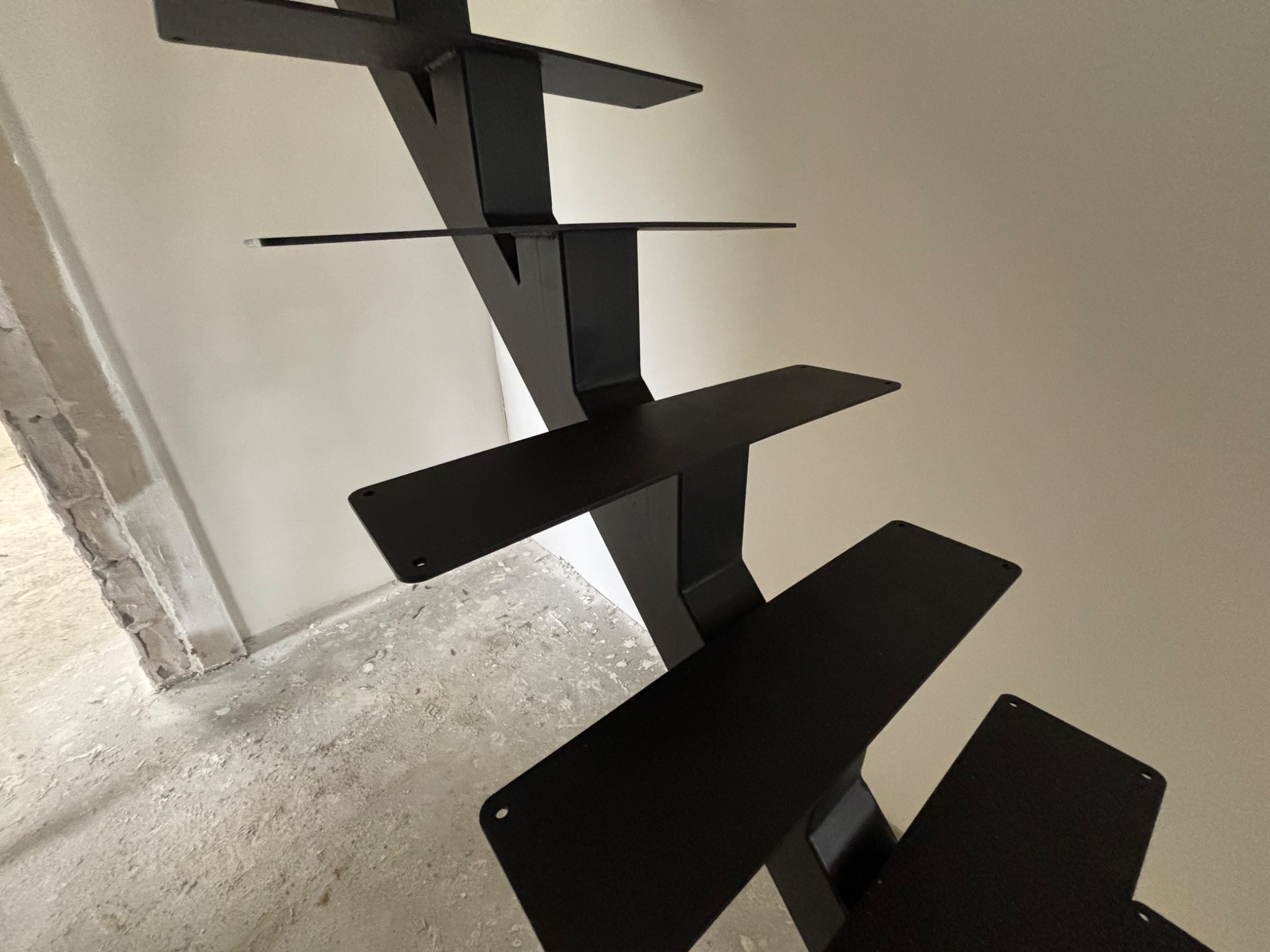 Surowe, nowoczesne schody metalowe w czarnym macie, widok z dołu, ukazujący minimalistyczną konstrukcję i surowy stan wykończenia wnętrza.