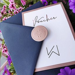 NOKO-CREATE PATRYK WOJEWODZIC - Elegancki voucher z pieczęcią lakową i granatową kopertą, otoczony kwiatami. Minimalistyczny design z napisem 'Voucher' i inicjałami.