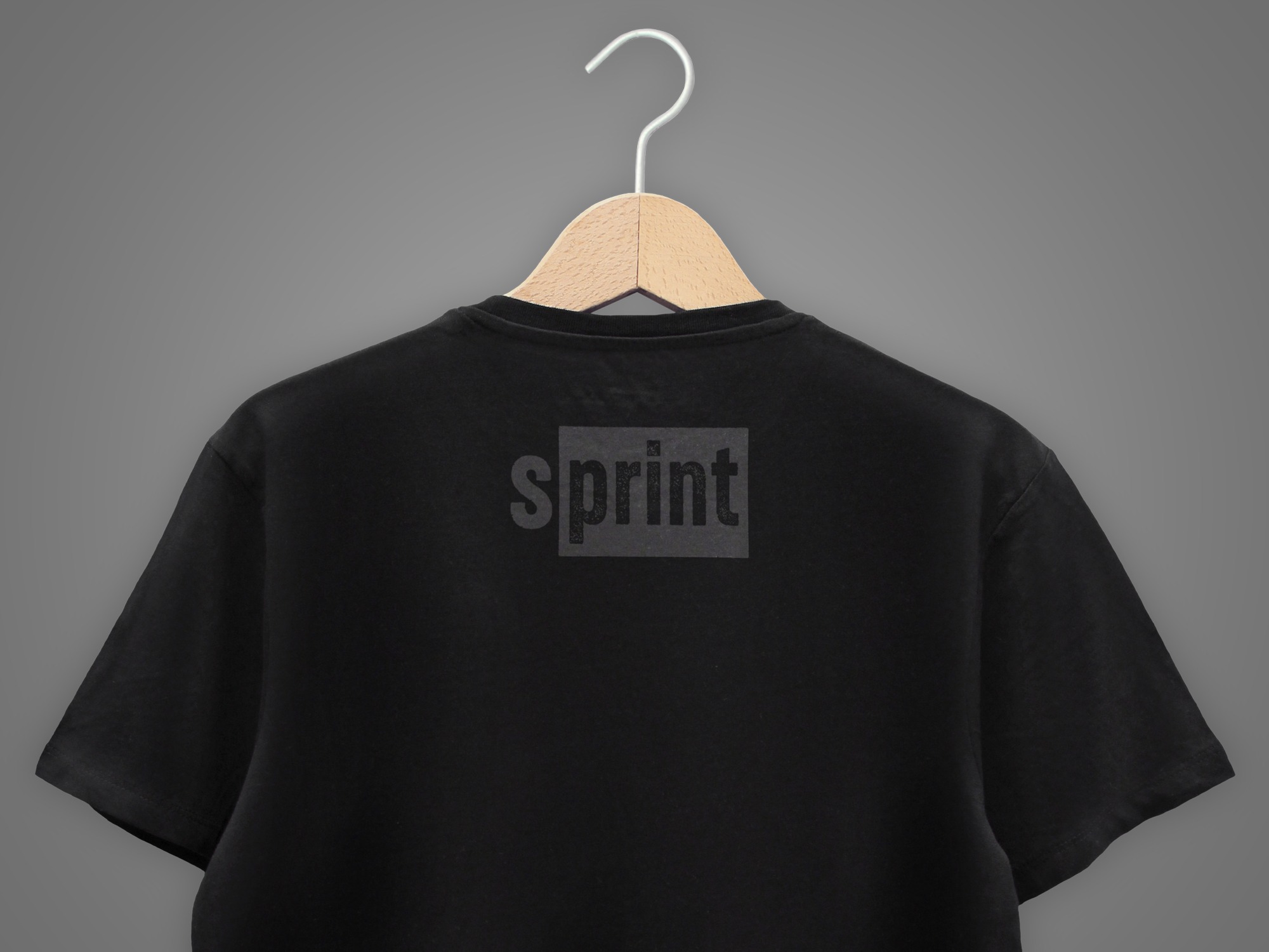 Czarna koszulka z nadrukiem 'sprint' zawieszona na drewnianym wieszaku na tle szarego studia. Widok z tyłu, skupiony na subtelnym, tonalnym logo.