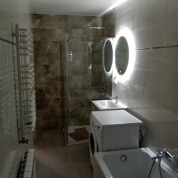 Igor Sobera - Wykończona łazienka z wanną, pralką zabudowaną pod umywalką, grzejnikiem drabinkowym i kabiną prysznicową z mozaiką w odcieniach beżu i brązu.