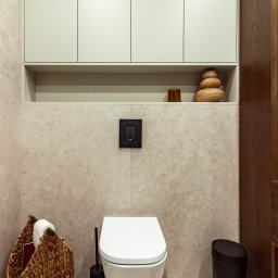 OiKa Studio Aleksandra Kośmider - Nowoczesna toaleta podwieszana w jasnej łazience w Olkuszu. Nad nią szafki i półka z dekoracjami. Kosz z wikliny i czarne akcesoria.