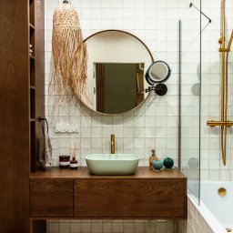 OiKa Studio Aleksandra Kośmider - Nowoczesna łazienka z drewnianą szafką pod umywalką, okrągłym lustrem i plecioną lampą. Białe płytki z kremową fugą, złota armatura, minimalistyczny design.