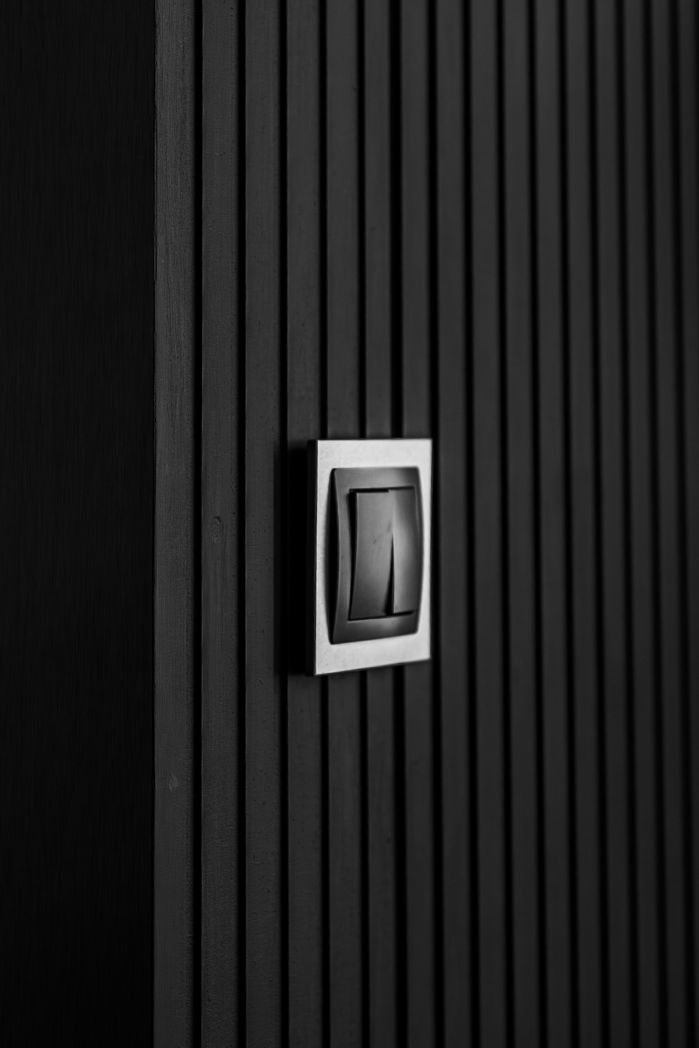 Minimalistyczny czarny włącznik światła z metalową ramką na ścianie z pionowych desek. Nowoczesny design, ciemne wnętrze, detal wykończenia.