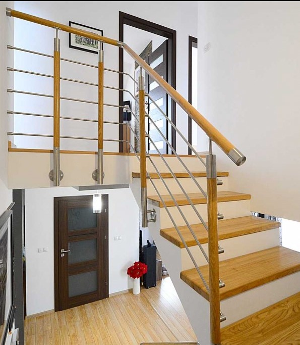 Nowoczesna balustrada schodowa z drewnianymi poręczami i stalowymi linkami, zamontowana w jasnym wnętrzu domu z drewnianymi schodami i podłogą.