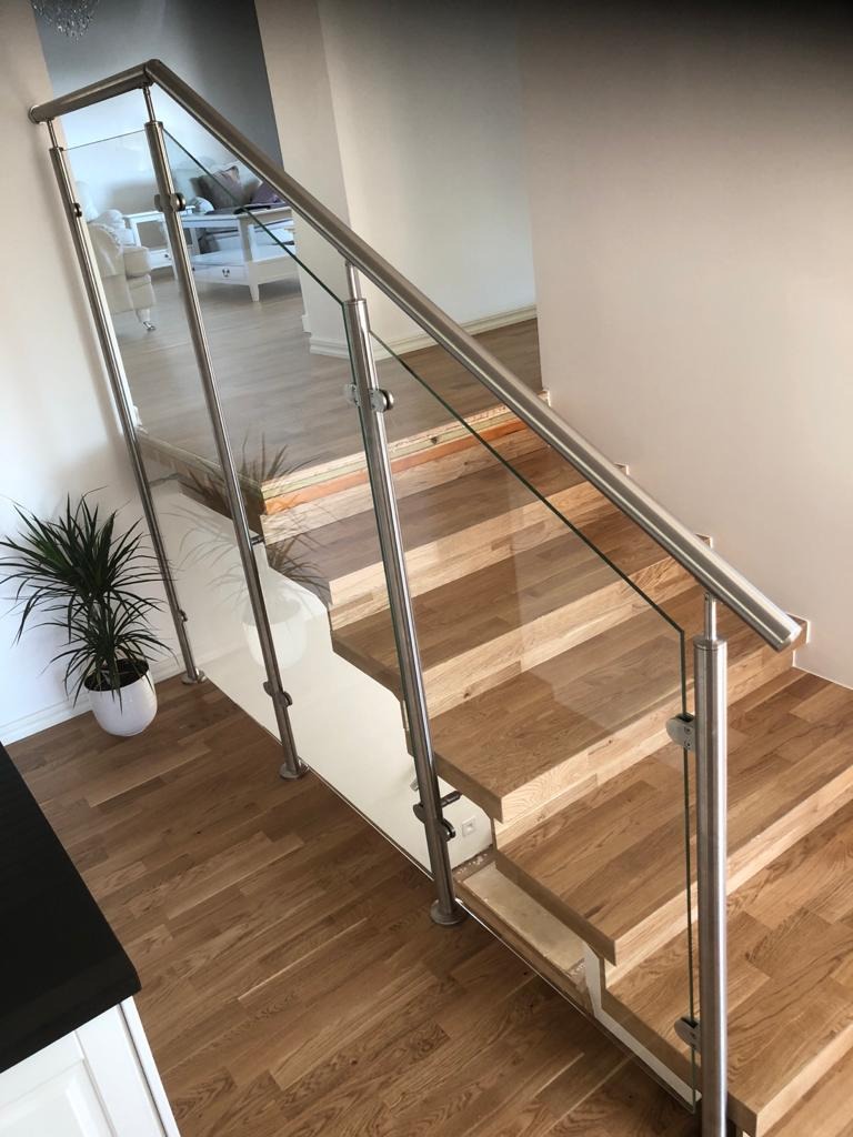 Nowoczesne schody z drewnianymi stopniami i szklaną balustradą z elementami ze stali nierdzewnej. Widok z góry, naturalne oświetlenie.