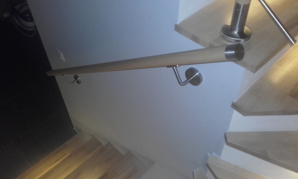 Drewniana poręcz schodowa z metalowymi uchwytami, widok od dołu, schody drewniane, jasne ściany. Minimalistyczny design poręczy.