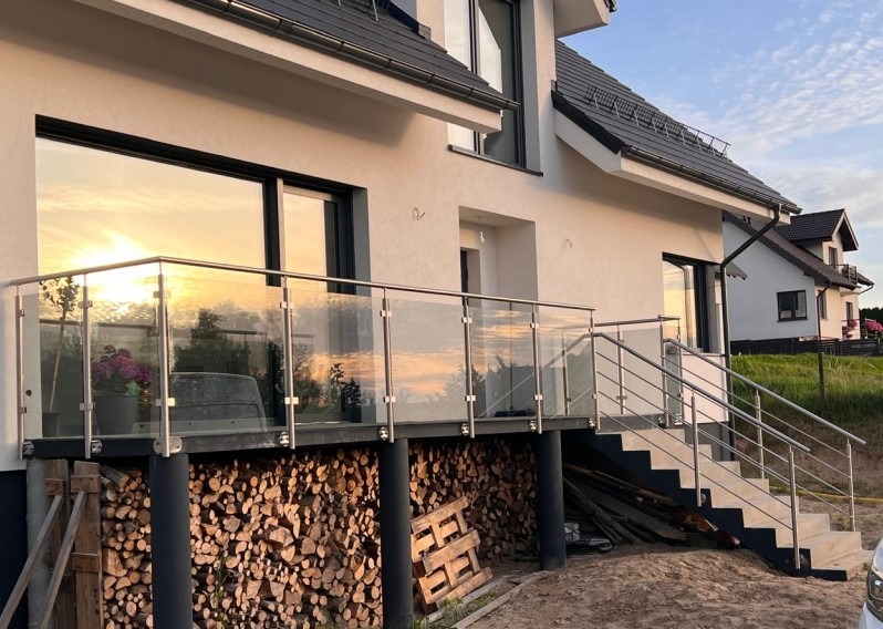 Nowoczesna balustrada szklana z elementami ze stali nierdzewnej na balkonie domu jednorodzinnego z widokiem na zachód słońca odbijającym się w szybach.