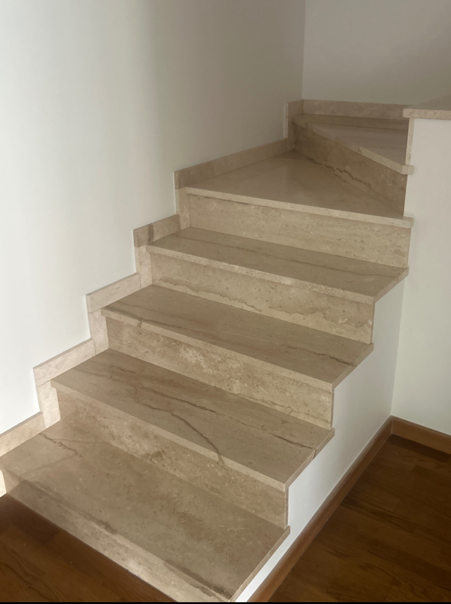 Wykończone schody wewnętrzne z beżowego marmuru, z widocznymi żyłami, prowadzące w górę, z drewnianą podłogą w tle i białymi ścianami.