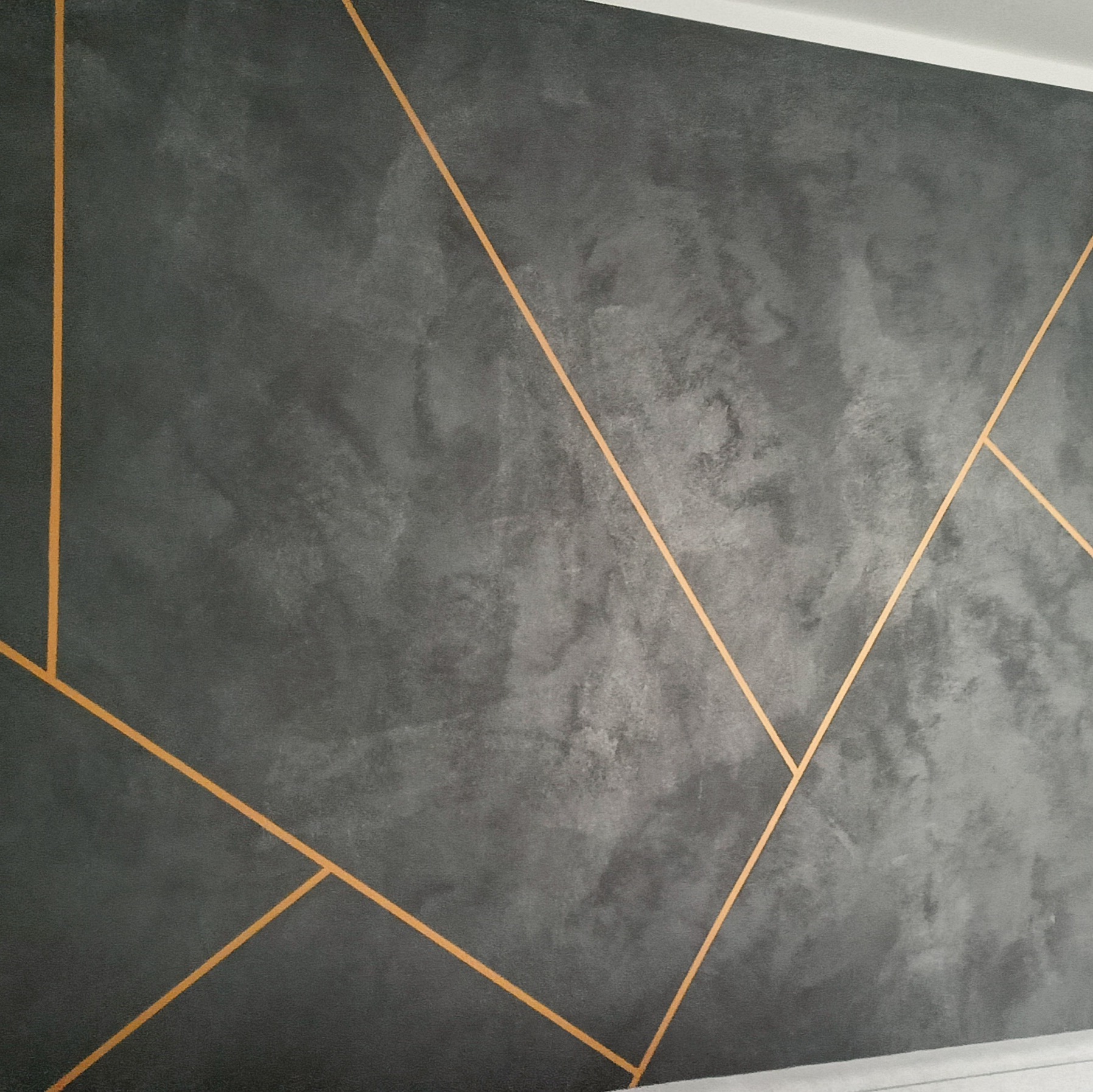 Szara ściana z dekoracyjnymi, złotymi liniami w Gorzowie Wielkopolskim. Efektowna faktura i nowoczesny design. Wykończenie wnętrza z dbałością o detale.